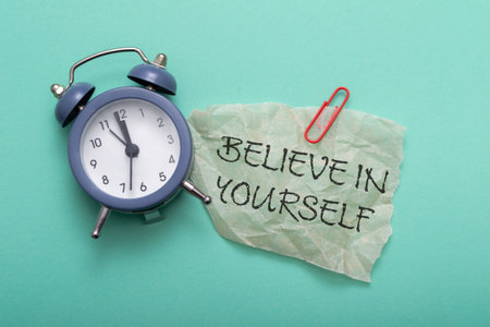 A clock with the hands on the number 12 and 6. A piece of paper with the words believe in yourself...