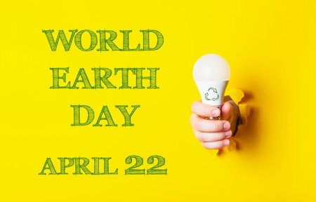 A person holding a light bulb with the words World Earth Day on the background. The image is yellow...