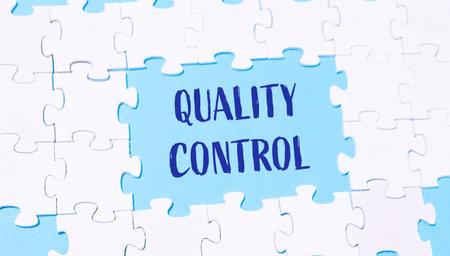 A puzzle with the word quality control written in blue. The puzzle is made up of white pieces and is...