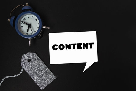 A blue alarm clock sits on a black background with the word content written in white. The clock is...