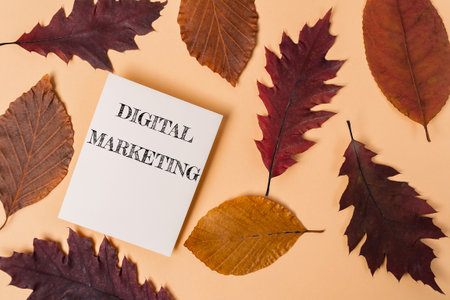 A white piece of paper with the word digital marketing written on it is placed on top of a pile of leavesの写真素材