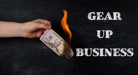 A hand holding a dollar bill with the words Gear Up Business written below it. Concept of starting a...