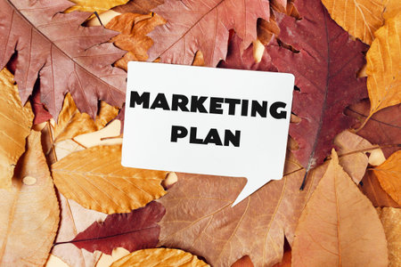 A white sign with the word marketing plan written on it is placed on top of a pile of autumn leaves