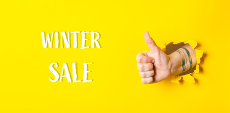 A hand is giving a thumbs up in front of a yellow background with the words Winter Sale written...