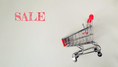 A shopping cart with the word Sale written on it. The cart is red and silver. The image has a...