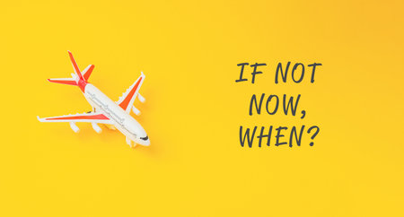 A small airplane is on a yellow background with the words If not now, when written below itの写真素材