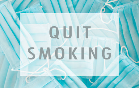 A blue sign with a white border that says Quit Smoking. The sign is surrounded by blue surgical masksの写真素材