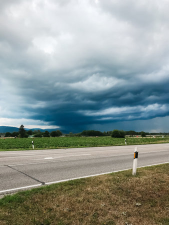 A storm is brewing in the sky above a road. The sky is dark and cloudy, and the road is empty