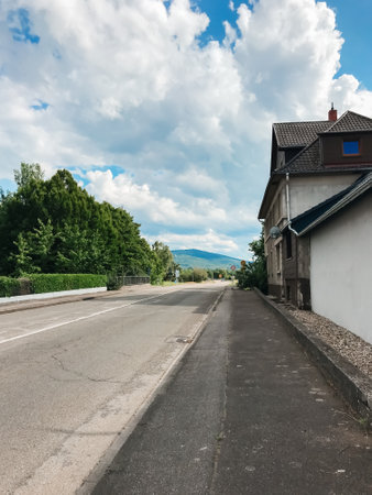 A street with a house on the right side. The street is empty and the sky is cloudyの写真素材