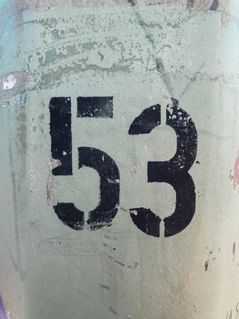 A black and white number 53 is written on a green surface. The number is surrounded by a black...