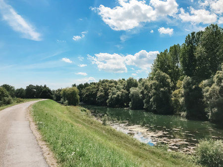 A road with a river running alongside it. The sky is blue and there are some clouds