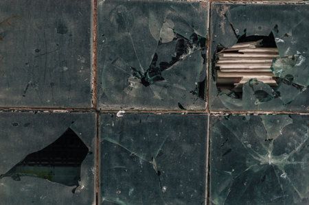 A broken window with a hole in it. The window is made of glass and is shattered.