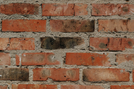 A brick wall with a few missing bricks. The wall is brown and red in color. The wall is old and has...