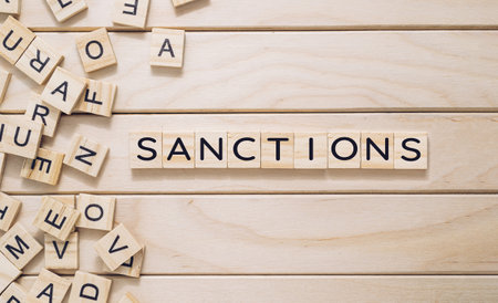 A wooden board with a jumble of letters scattered across it. The letters spell out the word sanctions in a crossword-like pattern. Concept of confusion and disarrayの写真素材