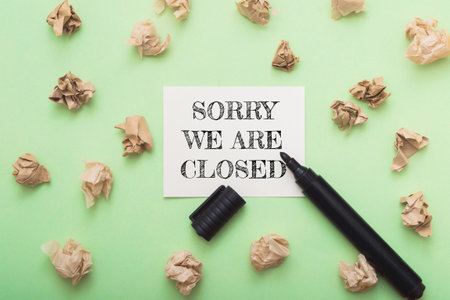 Sorry we are closed sign on a green background with a marker. The sign is written in black and is placed on top of a pile of paperの写真素材