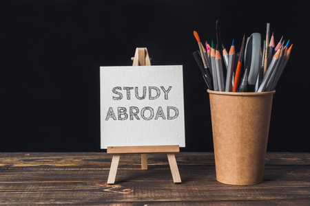 A white sign that says Study Abroad is on a wooden table. A cup of pencils is next to the signの写真素材