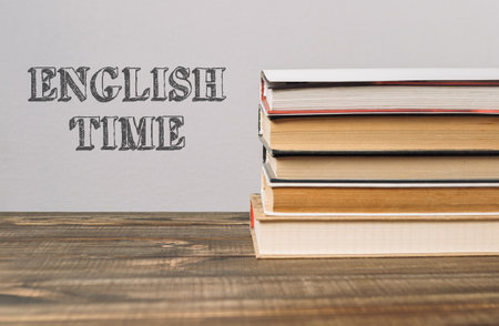 A stack of books with the word English Time written on top. The books are piled on top of each other on a wooden tableの写真素材