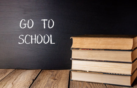 A stack of books with the words Go to School written on a chalkboard. The books are arranged in a pyramid shape, with the top book being the largest and the bottom book being the smallestの写真素材