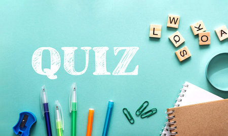 A green and blue background with a white word quiz written in white. There are several pens and pencils on the table, and a stack of booksの写真素材