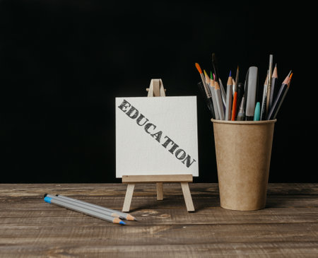 A white board with the word education written on it. A wooden stand holding a white board and a cup of pencilsの写真素材