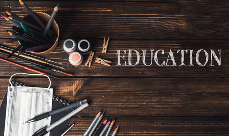 A wooden table with a bowl of pencils, a bottle of paint, and a pair of scissors. The word is written on the tableの写真素材