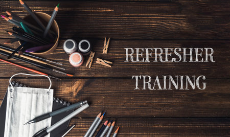 A wooden table with a bowl of colored pencils and a bottle of paint. The words Refresher Training...