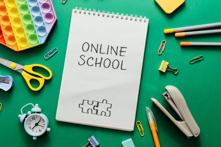 A notebook with the words Online School written on it. The notebook is surrounded by various school supplies such as scissors, a stapler, a clock, and a pencilの写真素材