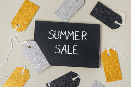 A black sign with the word Summer Sale written on it. There are many tags with glitter on them surrounding the signの写真素材