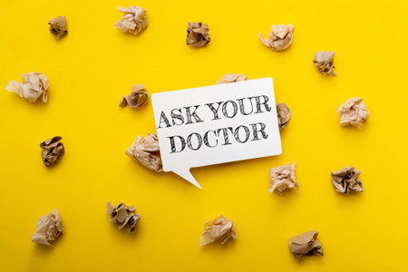 A yellow background with a white sign that says Ask Your Doctor. The sign is surrounded by shredded paperの写真素材
