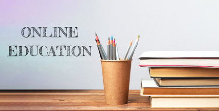 A wooden table with a cup of pencils and a stack of books. The words online education are written on the tableの写真素材