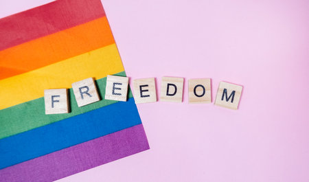 A rainbow flag with the word freedom written in wooden blocks. The flag is on a pink backgroundの写真素材