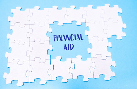 A jigsaw puzzle with the word financial aid written in the middle. The puzzle is incomplete, with pieces missing, and the blue background adds a sense of mystery and intrigue to the imageの写真素材