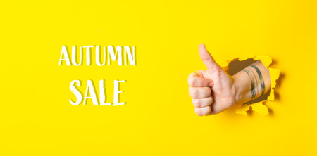 Hand is giving a thumbs up in front of a yellow background with the words Autumn Sale written below itの写真素材