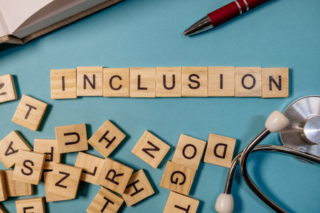 A wooden crossword puzzle with the word inclusion written across the top. The puzzle is scattered with various letters, and a pen is placed on the right side of the puzzleの写真素材
