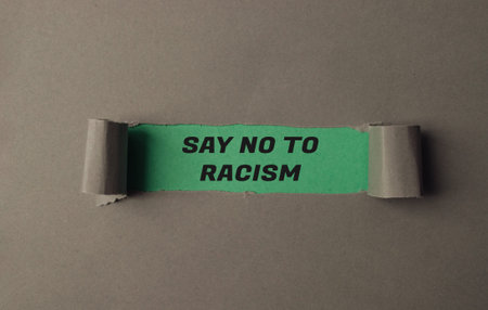 Torn piece of paper with the words Say No to Racism written on it. The paper is green and has a...