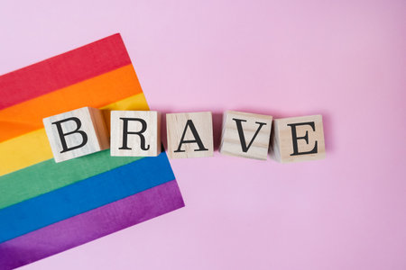 Rainbow flag and a wooden block with the word BRAVE written on it. The flag is colorful and vibrant, while the wooden block is simple and straightforwardの写真素材