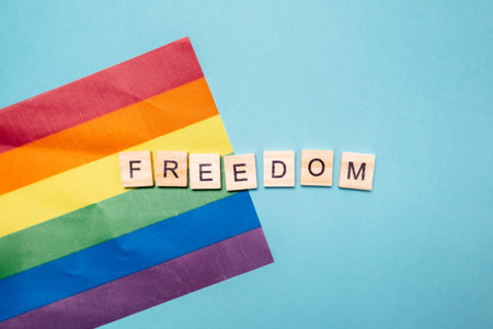 Rainbow flag with the word freedom written in wooden blocks. The flag is on a blue backgroundの写真素材