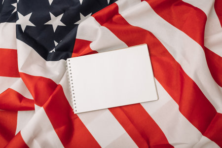 A white notebook is placed on top of a red and white American flag. The flag is spread out on a table, and the notebook is positioned in the center of the flagの写真素材