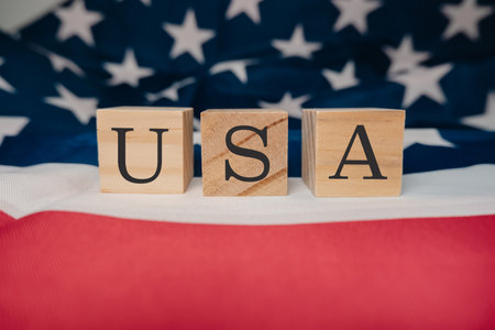 A wooden block with the letters USA written on it. The block is placed on top of a red and white American flag. The flag is spread out, covering a large portion of the backgroundの写真素材