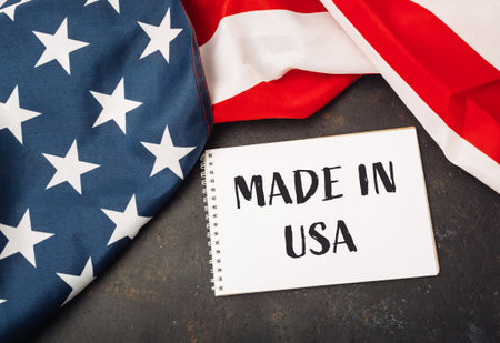 Made in USA is written on a white piece of paper. The paper is placed on top of a red, white, and blue American flagの写真素材