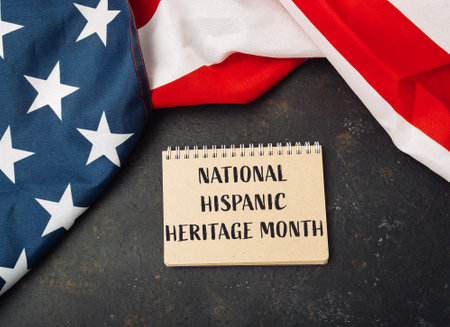National Hispanic Heritage Month is written on a notebook. The notebook is placed on top of a red and white American flagの写真素材