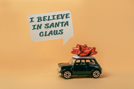 A green toy car with a red bow on top of it. The car is on a yellow background. The words are written above the carの写真素材