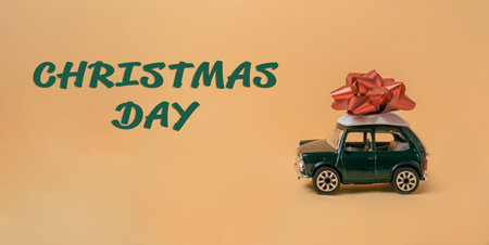 A green toy car with a red bow on top of it. The car is on a yellow background with the words Christmas Day written below itの写真素材
