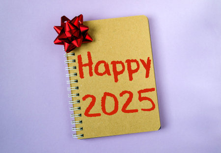 A spiral notebook with a red bow on top and the words Happy 2025 written in red. The notebook is on...