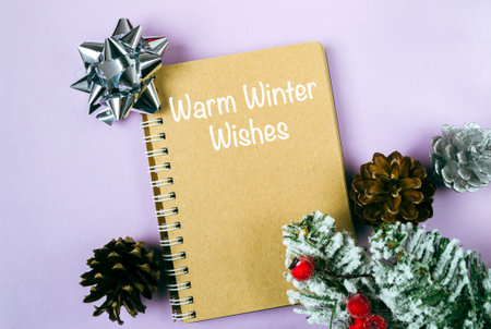 A notebook with a Christmas tree on top of it. The notebook is open to a blank page with the words warm winter wishes written on itの写真素材