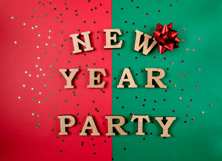 A green and red background with a red bow on top of the word New Year Party. The letters are made of wood and are scattered around the backgroundの写真素材