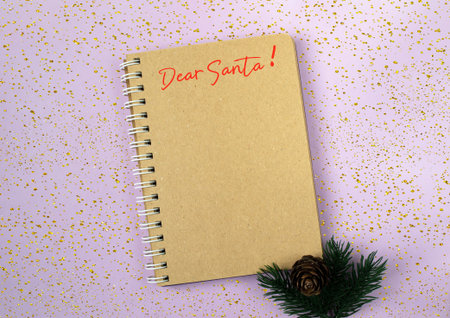 A brown spiral notebook with a red pen on it that says Dear Santa. The notebook is sitting on a...
