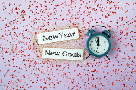A blue alarm clock sits on a pink background with the words New Year, New Goals written on a white...