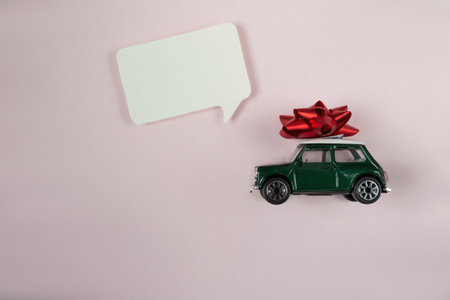 Green toy car with a red bow on top of it. The car is on a pink backgroundの写真素材