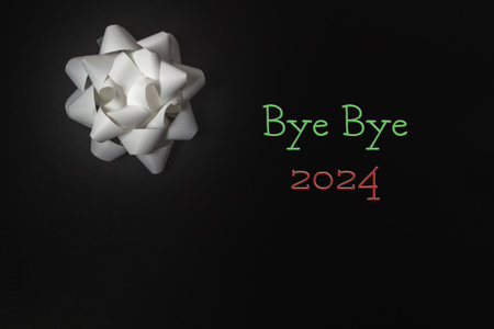 White bow with the words bye bye 2024 written in red and green. The bow is on a black backgroundの写真素材